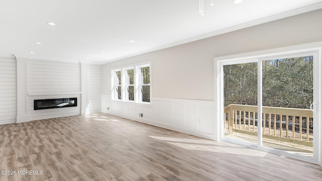 unfurnished living room with a wainscoted wall, recessed lighting, ornamental molding, a glass covered fireplace, and wood finished floors