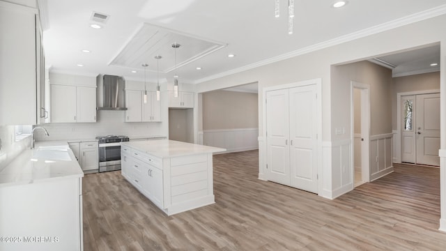 kitchen with visible vents, wainscoting, stainless steel gas stove, a sink, and wall chimney range hood