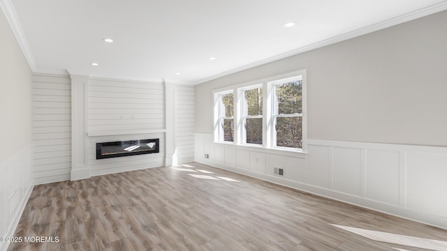 unfurnished living room with recessed lighting, wood finished floors, visible vents, ornamental molding, and a glass covered fireplace