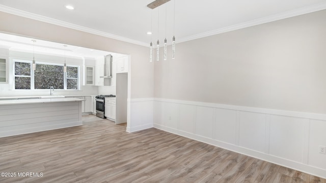 unfurnished dining area featuring a wainscoted wall, light wood-type flooring, and crown molding