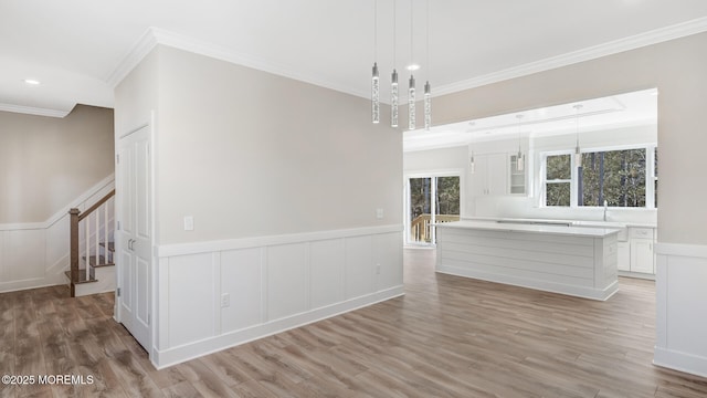 spare room featuring a wainscoted wall, light wood finished floors, recessed lighting, ornamental molding, and stairs