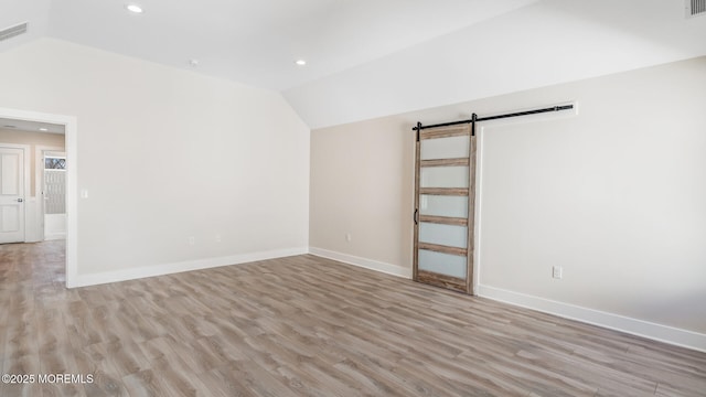 unfurnished room featuring light wood-type flooring, vaulted ceiling, baseboards, and a barn door