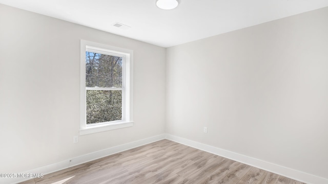 unfurnished room featuring light wood-style floors, a healthy amount of sunlight, visible vents, and baseboards