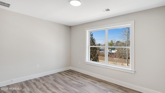 empty room with light wood-type flooring, visible vents, and baseboards