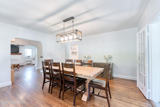 dining space with radiator, wood finished floors, baseboards, arched walkways, and ornamental molding