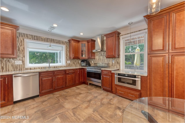 kitchen with pendant lighting, a sink, stainless steel appliances, wall chimney range hood, and decorative backsplash