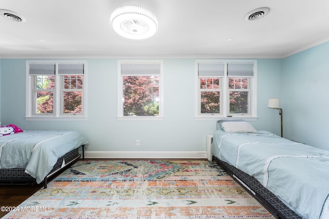 bedroom with visible vents, baseboards, wood finished floors, and ornamental molding