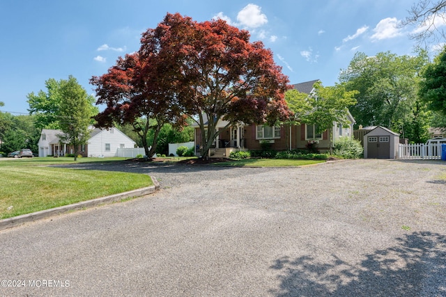 view of property hidden behind natural elements featuring fence, a storage shed, an outdoor structure, a front yard, and brick siding