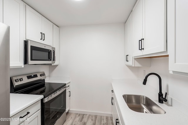 kitchen with stainless steel appliances, a sink, light countertops, and white cabinets