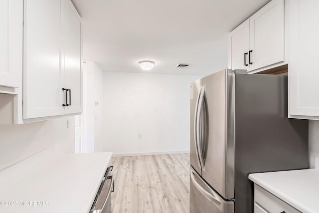 kitchen with light wood finished floors, visible vents, white cabinets, freestanding refrigerator, and light countertops