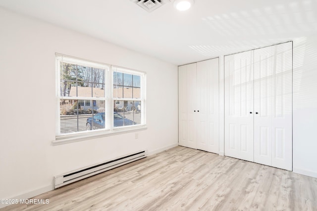 unfurnished bedroom featuring two closets, visible vents, baseboard heating, wood finished floors, and baseboards