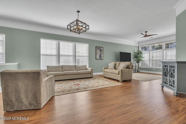 living area featuring baseboards, ornamental molding, wood finished floors, a textured ceiling, and ceiling fan with notable chandelier