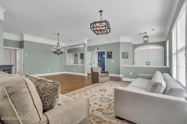 living room featuring baseboards, crown molding, a chandelier, and wood finished floors