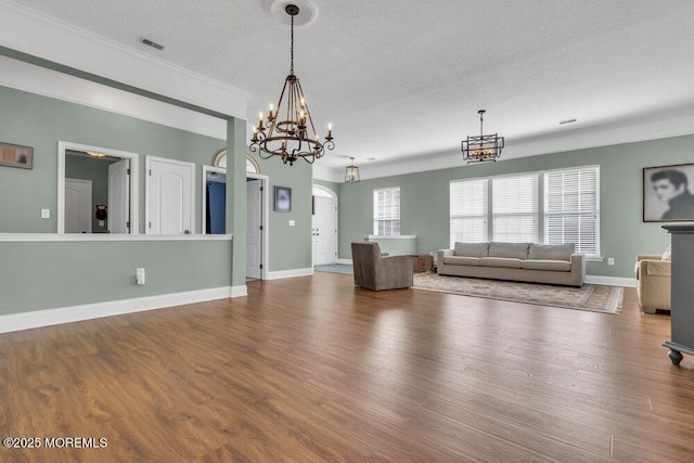 unfurnished living room featuring visible vents, a textured ceiling, wood finished floors, a chandelier, and baseboards