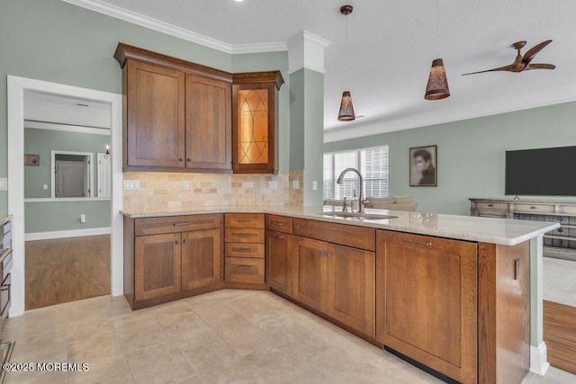 kitchen featuring brown cabinets, crown molding, tasteful backsplash, a sink, and a peninsula