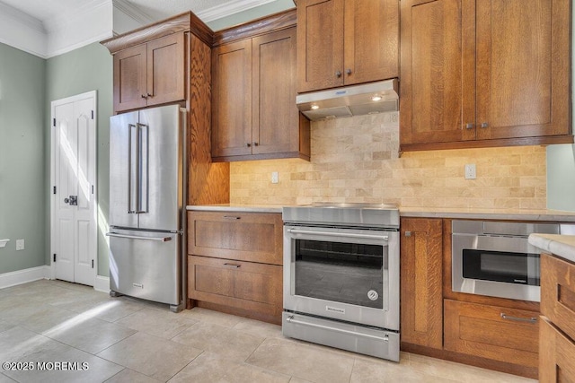 kitchen featuring under cabinet range hood, stainless steel appliances, light countertops, ornamental molding, and tasteful backsplash