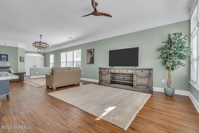 living area featuring ceiling fan with notable chandelier, baseboards, wood finished floors, and ornamental molding