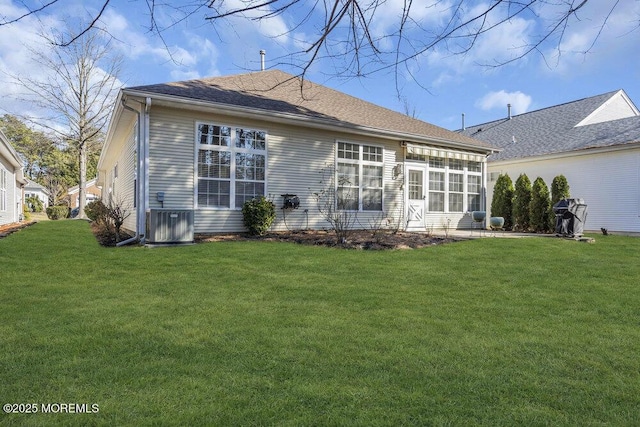 rear view of house with a shingled roof, a patio area, central AC, and a yard