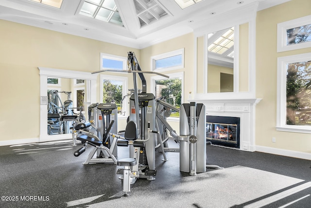 workout area with a glass covered fireplace, coffered ceiling, a towering ceiling, and baseboards