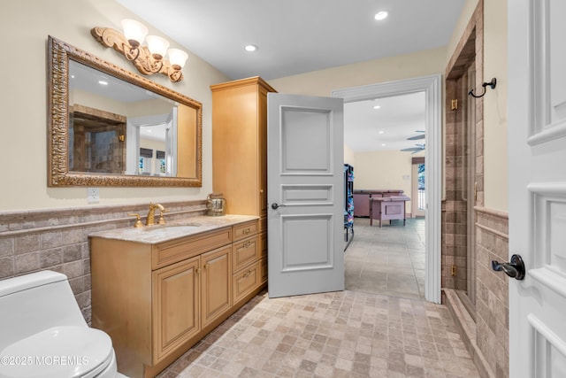 bathroom featuring vanity, a wainscoted wall, tile walls, toilet, and a shower with door