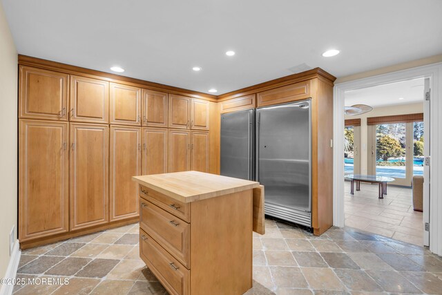 kitchen featuring stainless steel built in refrigerator, a kitchen island, stone tile flooring, recessed lighting, and butcher block counters