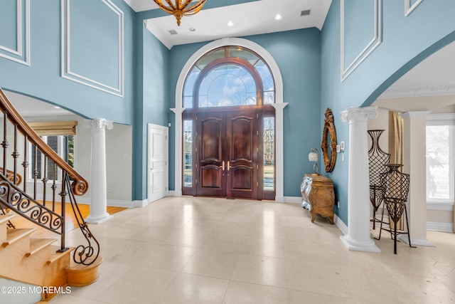 foyer entrance featuring decorative columns, baseboards, visible vents, and a towering ceiling