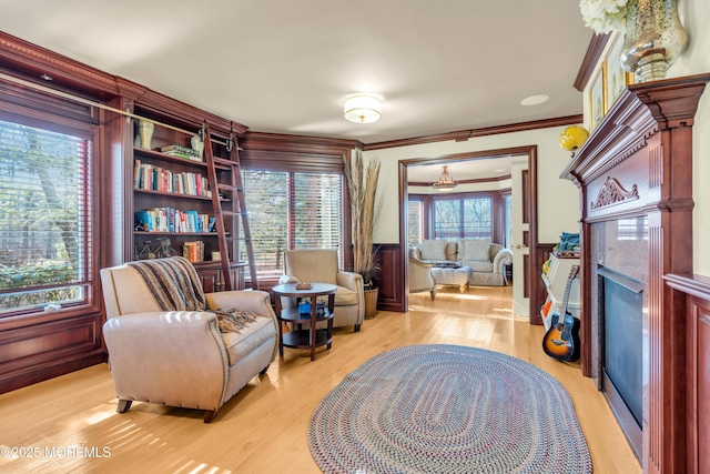 sitting room featuring wainscoting, a fireplace, crown molding, and light wood-style floors