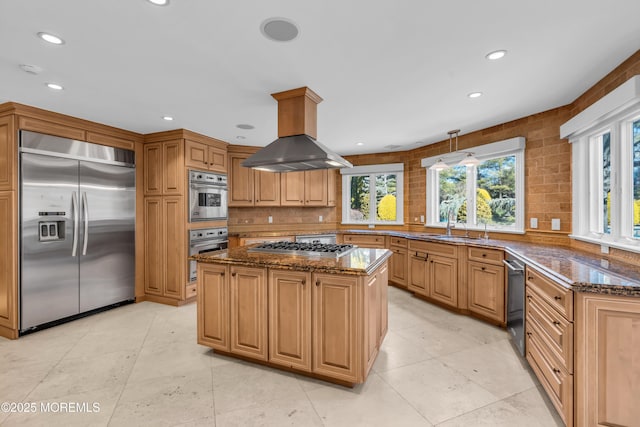 kitchen featuring tasteful backsplash, dark stone counters, appliances with stainless steel finishes, island range hood, and a sink