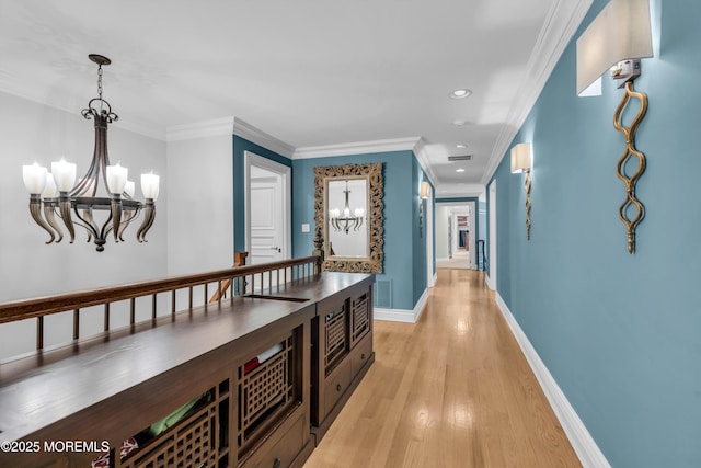 hall with a notable chandelier, light wood-style flooring, baseboards, and ornamental molding