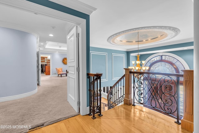 hall with a tray ceiling, ornamental molding, an upstairs landing, wood finished floors, and a notable chandelier