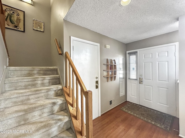 entryway featuring stairs, visible vents, a textured ceiling, and wood finished floors