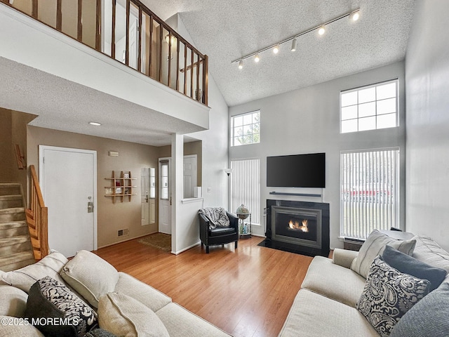 living room with a fireplace with flush hearth, a textured ceiling, wood finished floors, and a towering ceiling