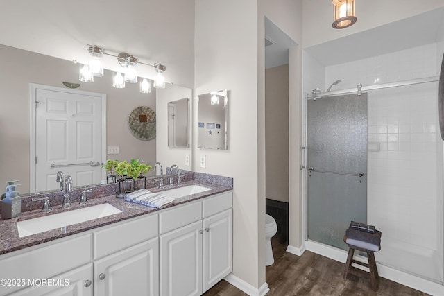 full bath featuring toilet, a stall shower, double vanity, and a sink