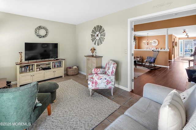 living area with baseboards, a notable chandelier, ornate columns, and tile patterned floors