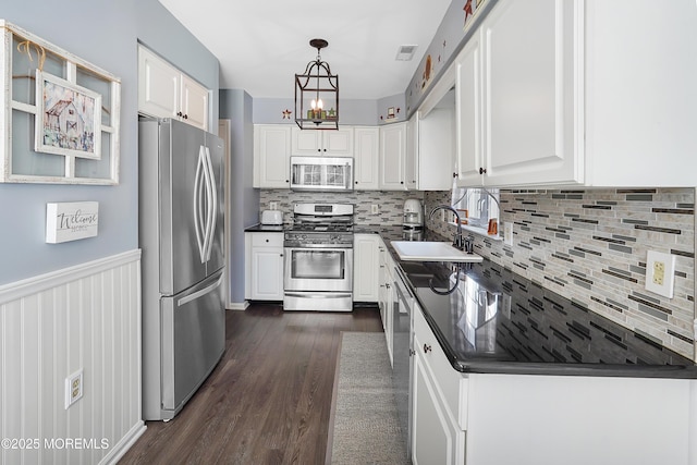 kitchen featuring dark wood finished floors, stainless steel appliances, dark countertops, white cabinetry, and a sink