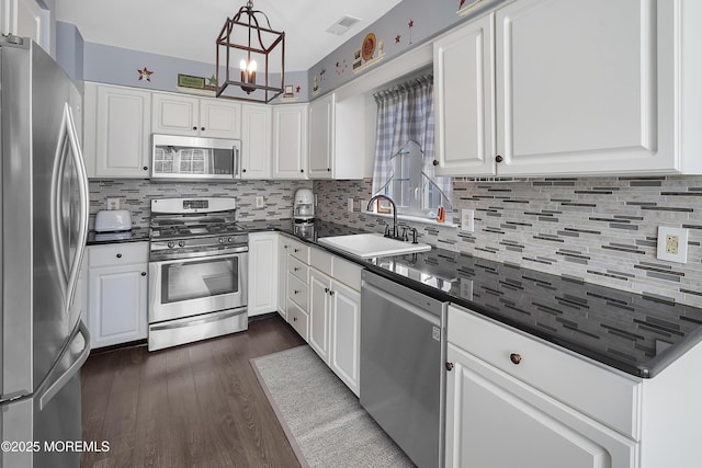 kitchen featuring dark countertops, dark wood-style flooring, stainless steel appliances, white cabinetry, and a sink