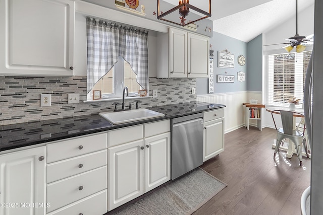 kitchen with dark countertops, a wainscoted wall, lofted ceiling, appliances with stainless steel finishes, and a sink