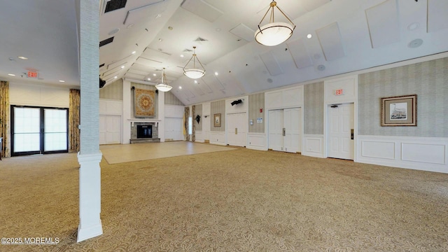 unfurnished living room with a fireplace with raised hearth, a decorative wall, carpet floors, wainscoting, and ornate columns