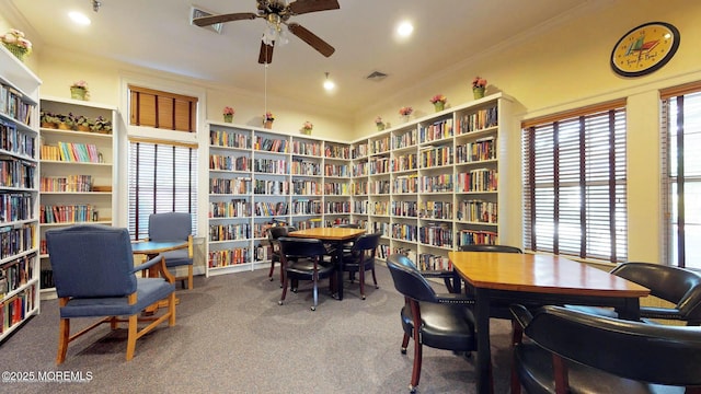 sitting room featuring visible vents, ceiling fan, crown molding, carpet floors, and bookshelves