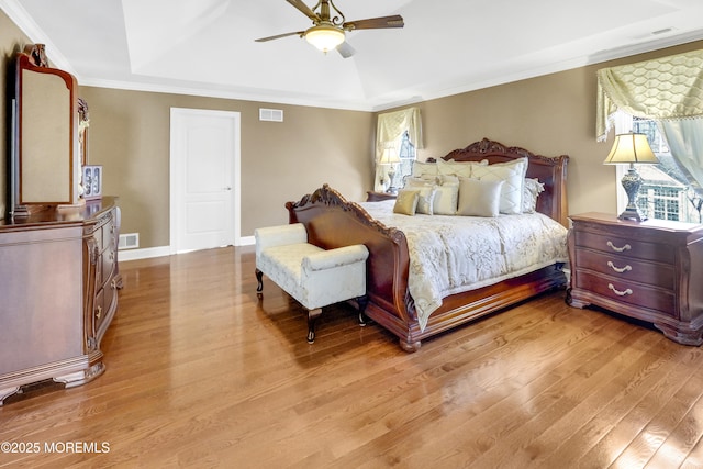 bedroom with light wood finished floors, ornamental molding, a raised ceiling, and visible vents