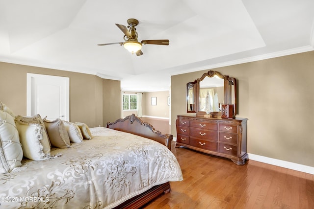 bedroom featuring a tray ceiling, a ceiling fan, ornamental molding, wood finished floors, and baseboards