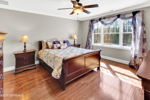 bedroom with wood finished floors, a ceiling fan, visible vents, baseboards, and ornamental molding