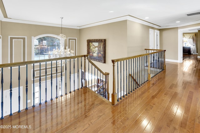 hallway with visible vents, wood-type flooring, an inviting chandelier, an upstairs landing, and a wealth of natural light