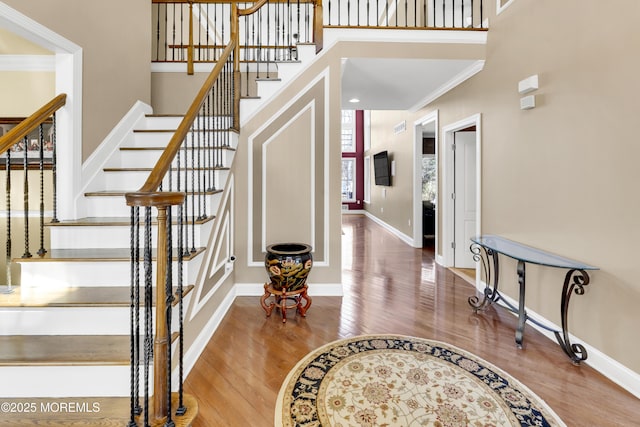 stairway with a towering ceiling, crown molding, baseboards, and wood finished floors