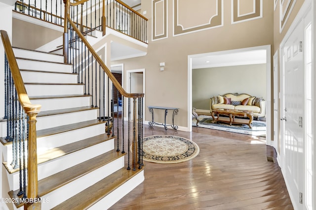 staircase featuring ornamental molding, a towering ceiling, baseboards, and hardwood / wood-style flooring