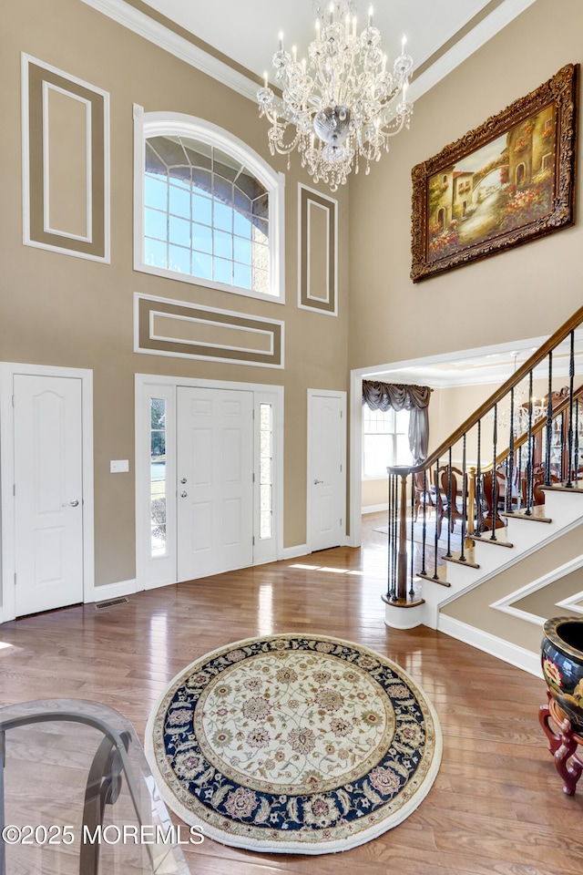 entrance foyer featuring baseboards, stairway, ornamental molding, wood finished floors, and a notable chandelier