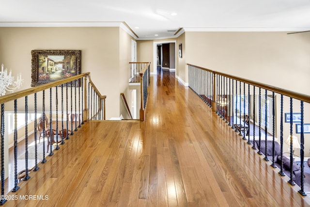 corridor featuring baseboards, wood-type flooring, crown molding, an upstairs landing, and recessed lighting