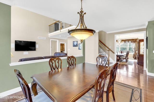 dining space featuring baseboards, visible vents, wood finished floors, stairs, and crown molding