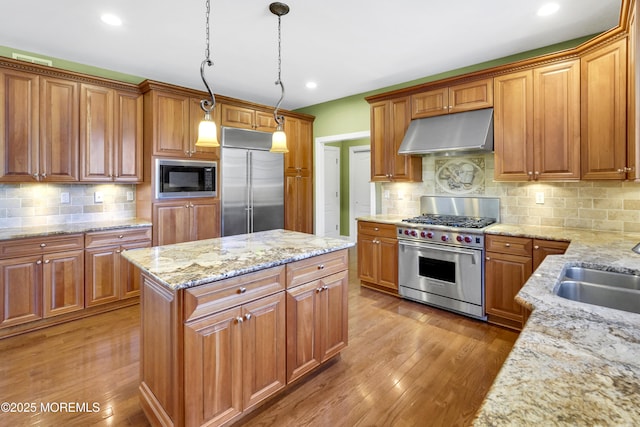 kitchen featuring built in appliances, under cabinet range hood, light wood-style floors, light stone countertops, and brown cabinetry