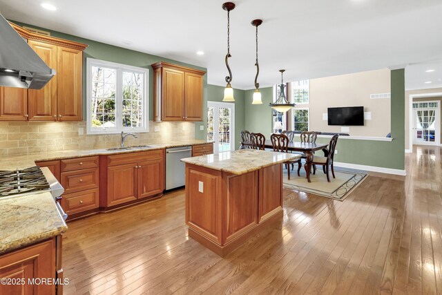 kitchen with light wood finished floors, tasteful backsplash, stainless steel dishwasher, a sink, and wall chimney exhaust hood